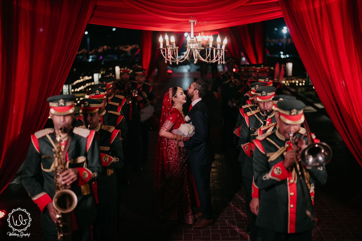 Elegant ballroom wedding reception with dramatic red lighting, crystal chandeliers, and ornate table settings.