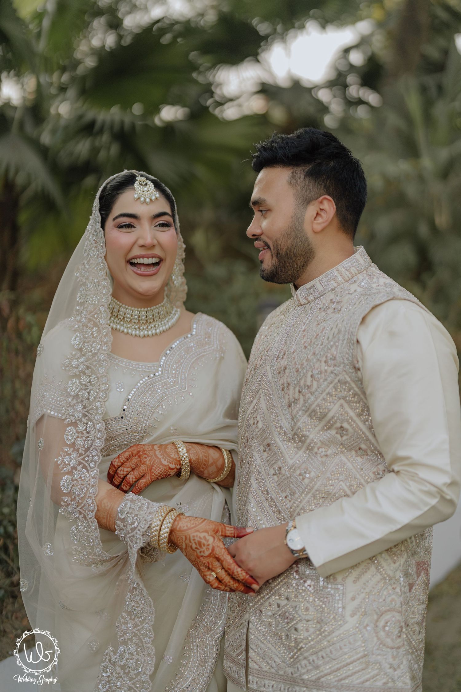 A couple in traditional South Asian wedding attire share joyful moments during an outdoor photoshoot.