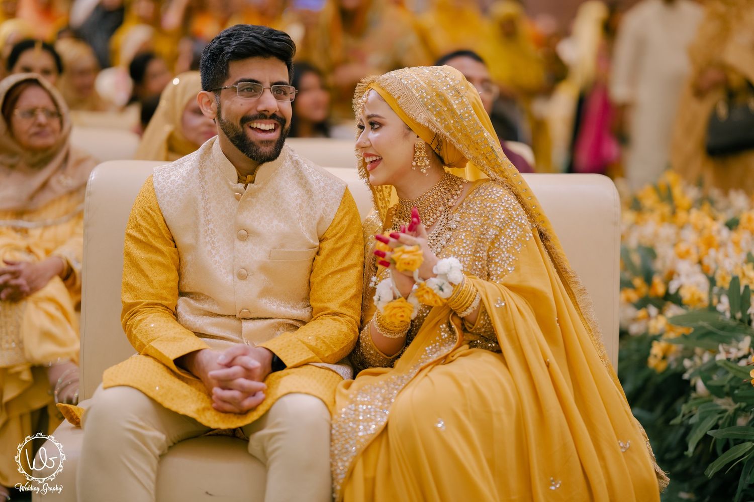 Joyful couple in matching yellow outfits sharing laughter during a traditional wedding celebration.