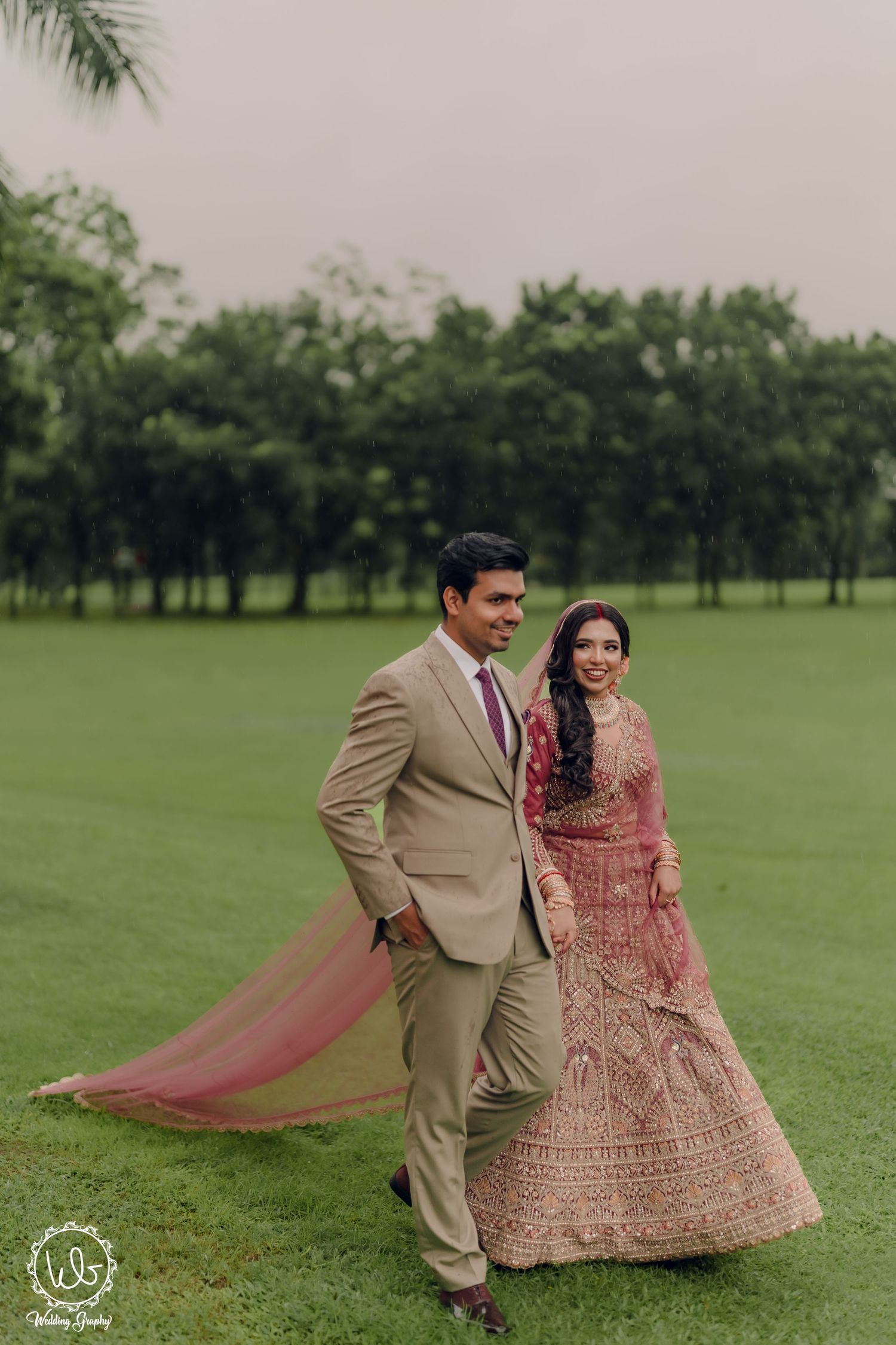 A couple in traditional South Asian wedding attire dances together on a lush green lawn.
