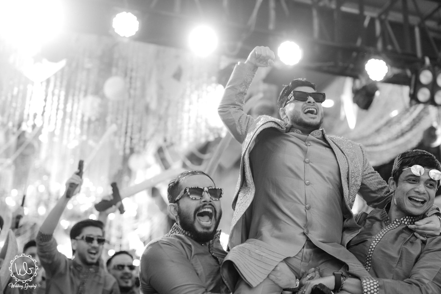 Black and white photo of wedding guests dancing and celebrating at a reception.