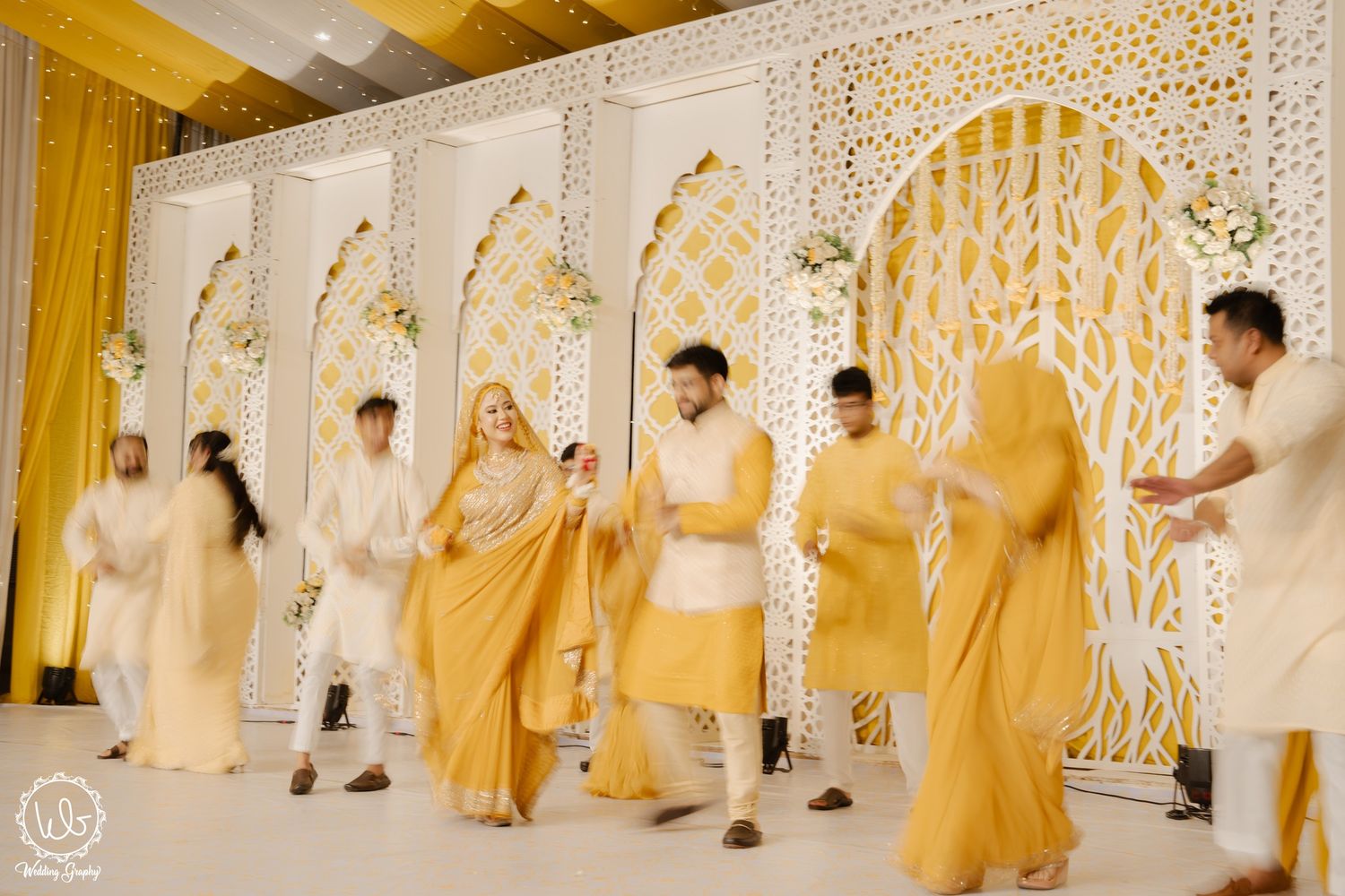 Wedding party in golden attire walking down decorated white hallway during traditional ceremony.
