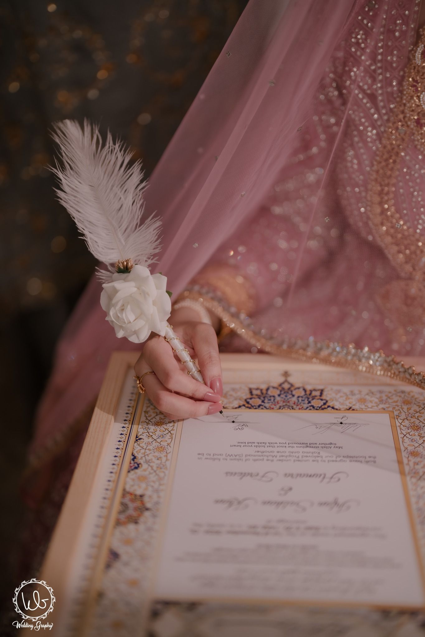 Close-up view of hands holding an elegant wedding invitation with ornate details against a pink sparkly background.