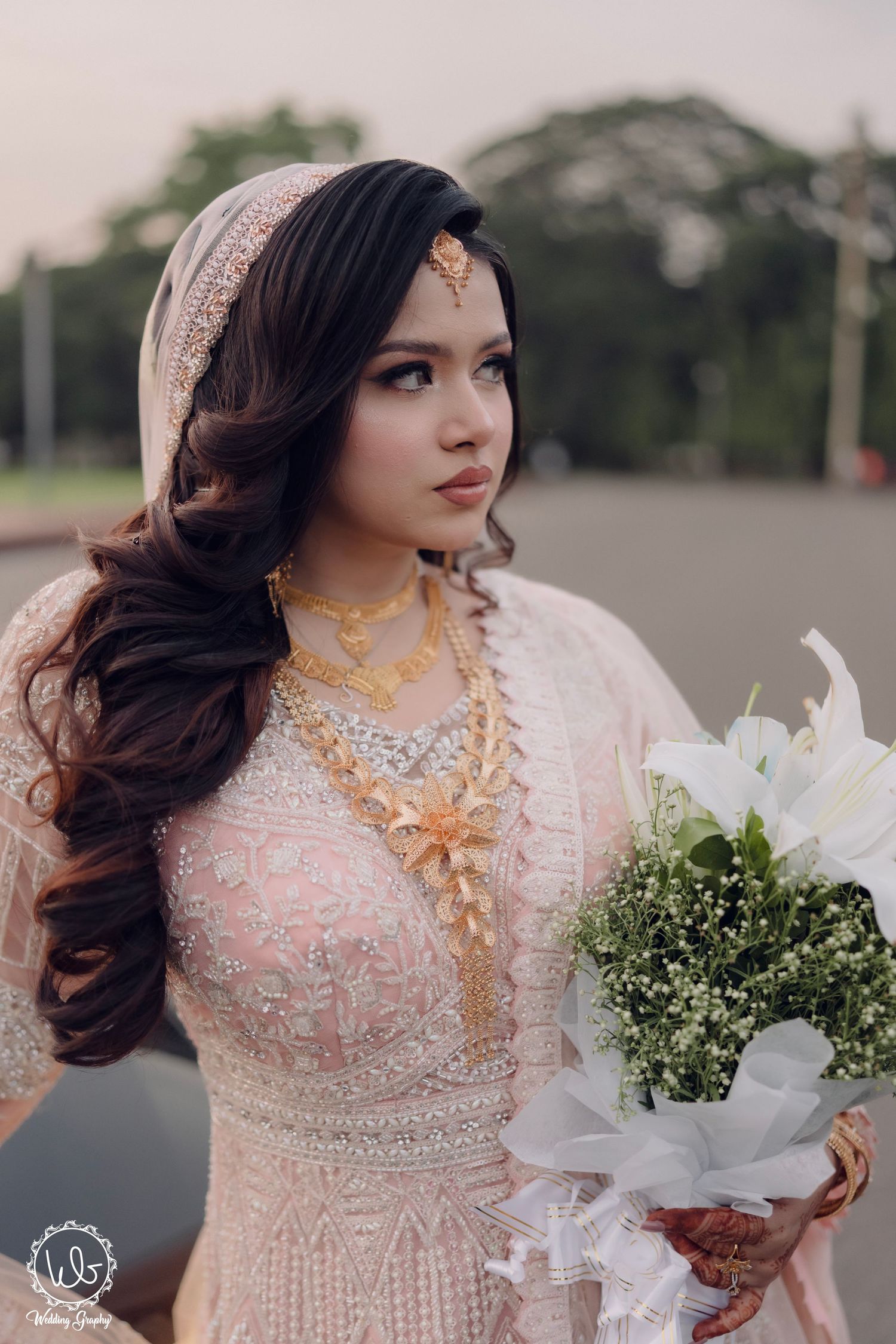 Bride in delicate pink embroidered dress holds white flower bouquet during outdoor photoshoot.