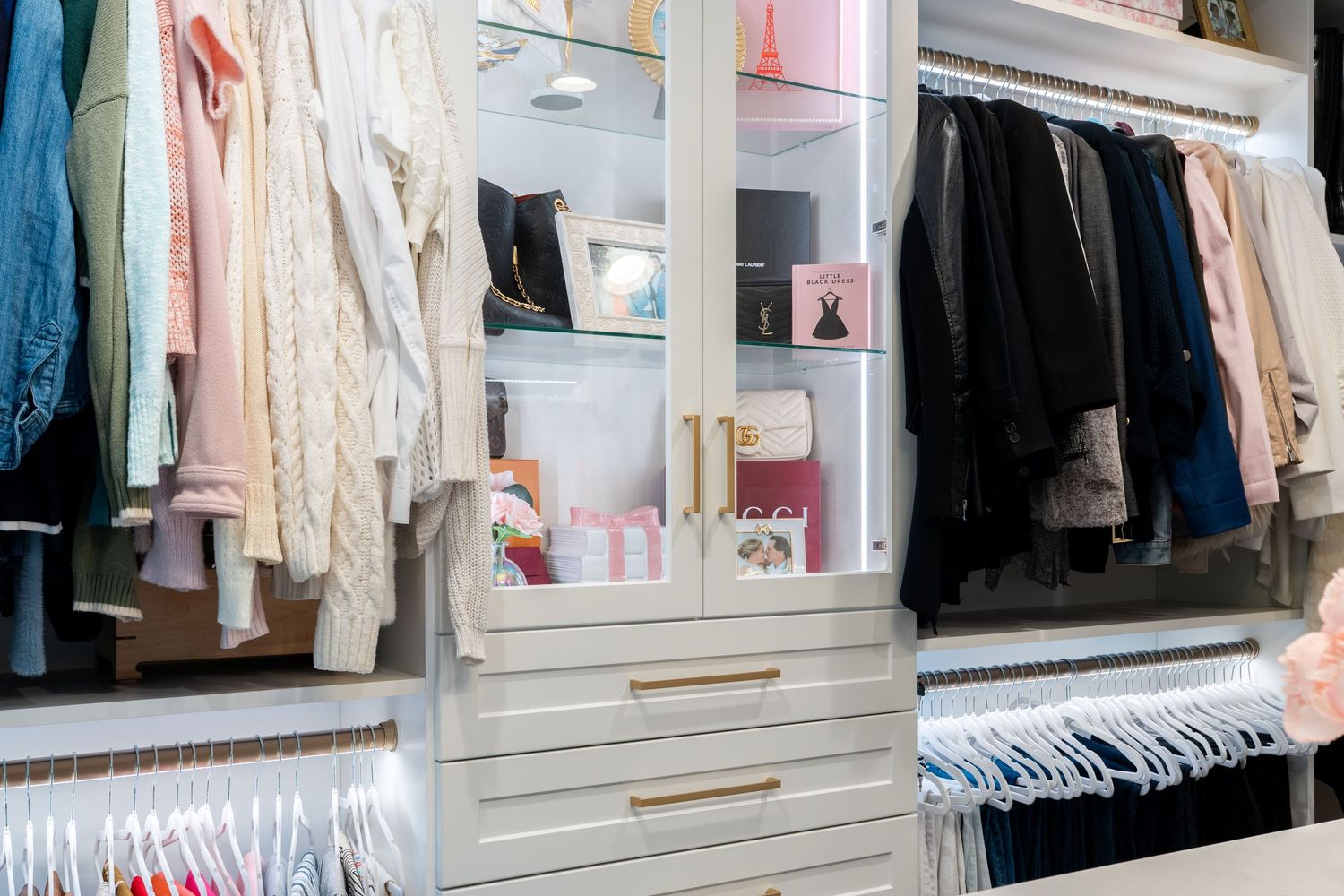 Elegant walk-in closet with white shelving, gold hardware, hanging clothes, and organized accessories on display.