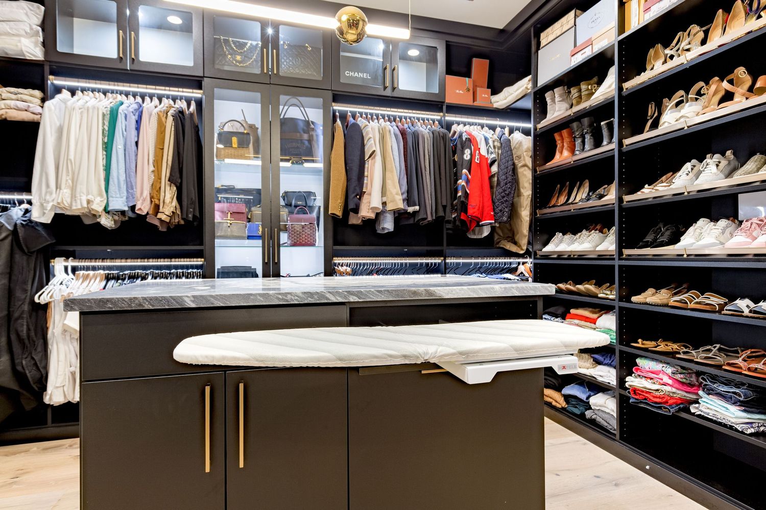 A modern walk-in closet with organized clothing racks, shoe shelves, and a central island with brass hardware.