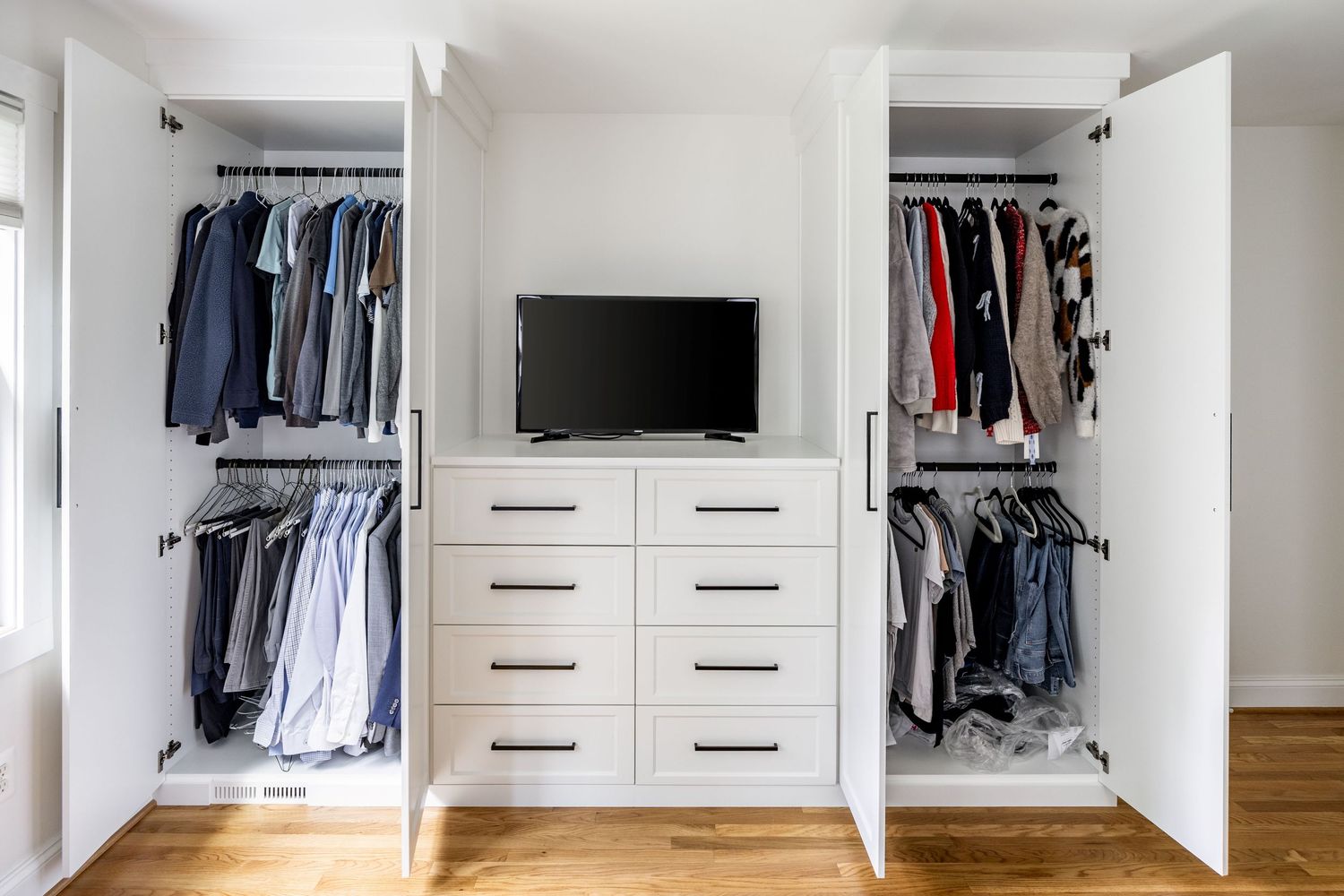 Modern white walk-in closet with built-in storage, clothing racks, and hardwood flooring in bright natural light.