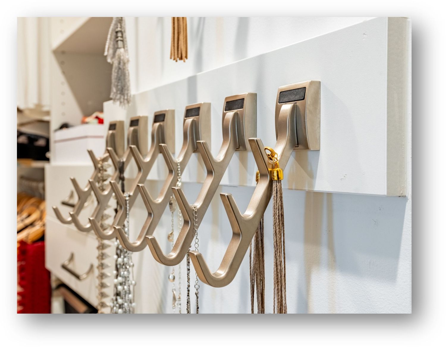 Silver wall-mounted hooks display jewelry and accessories on a white wall in an organized fashion.