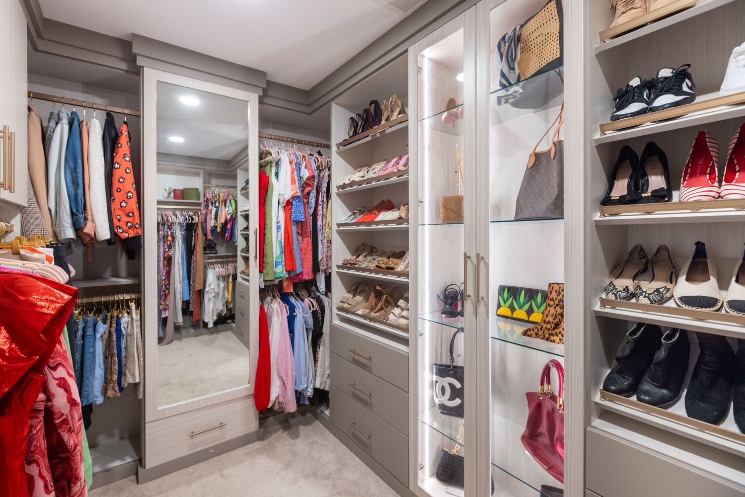 Modern walk-in closet with built-in white shelving displays organized shoes, clothes and accessories with bright lighting.