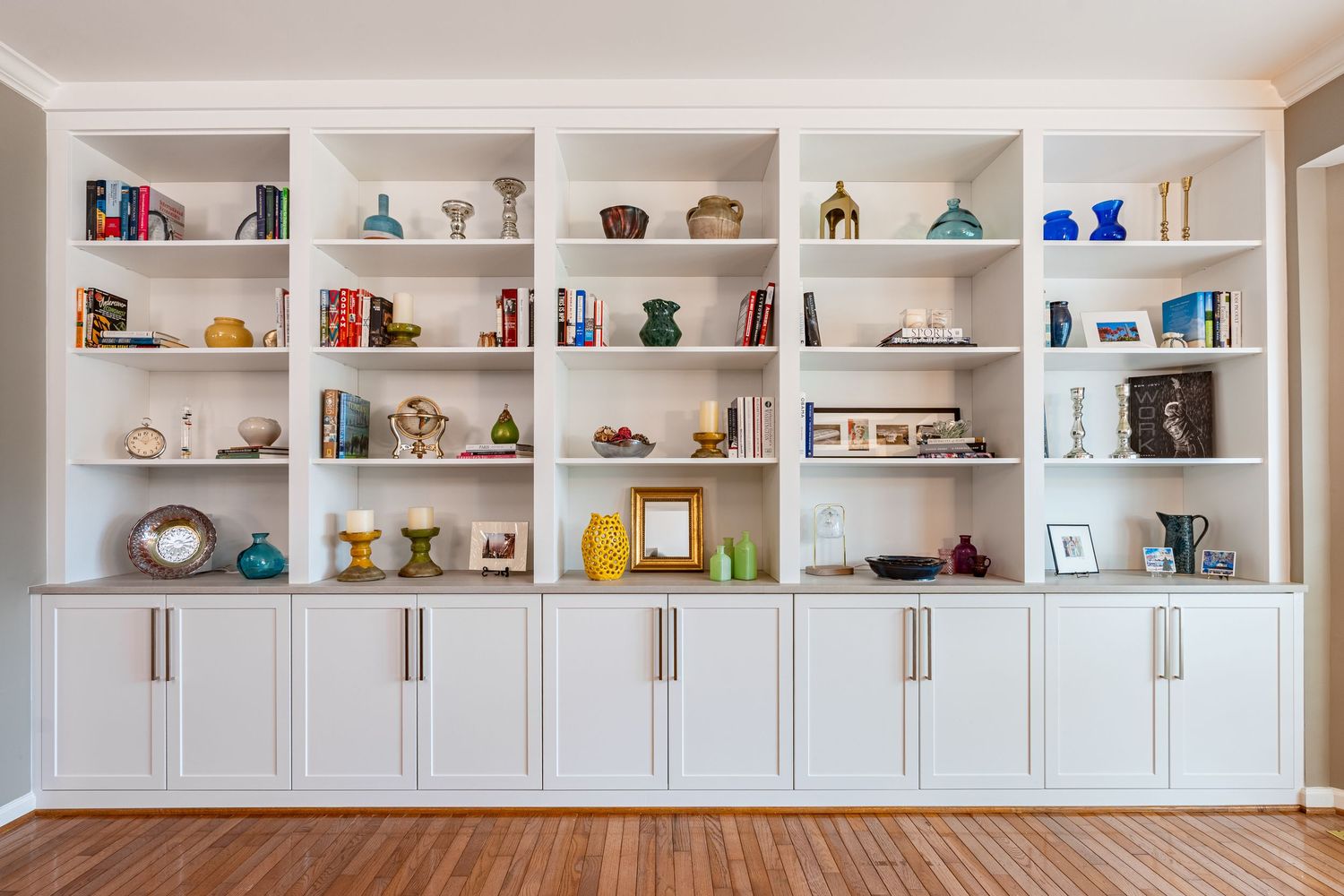 White built-in bookcase with decorative objects, books, and colorful vases displayed on shelves above cabinet storage.