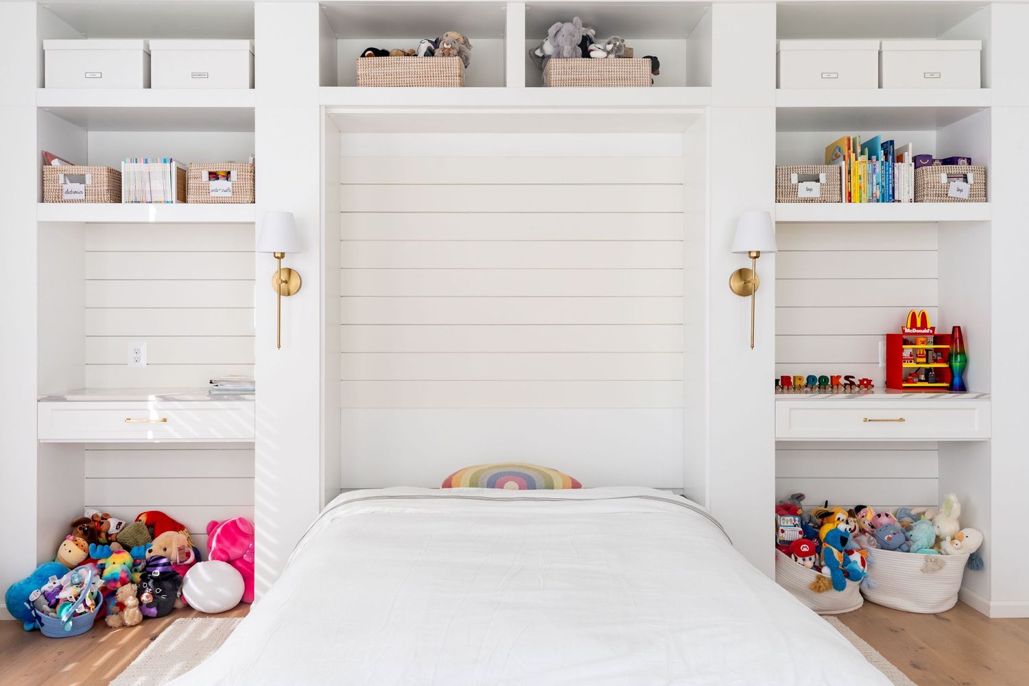 White floating shelves mounted on brick wall displaying books, toys, and decorative items in a modern nursery setting.