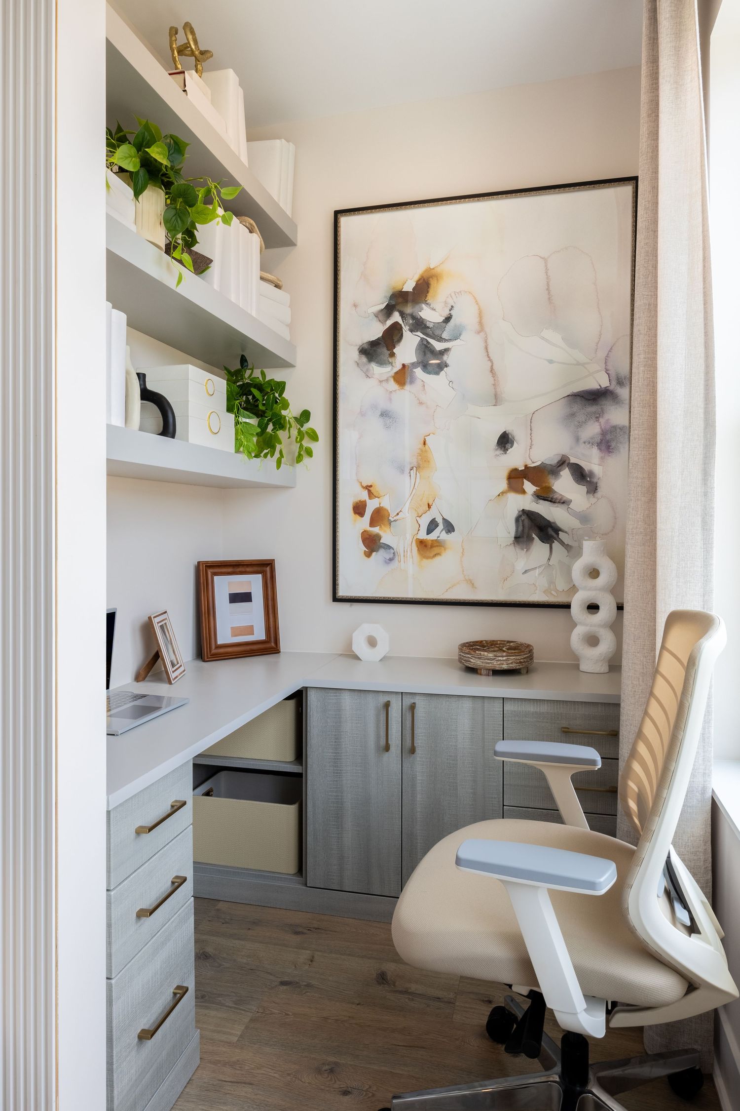 Modern home office space with grey cabinets, white walls, floating shelves, and artistic wall decor in a minimalist style.