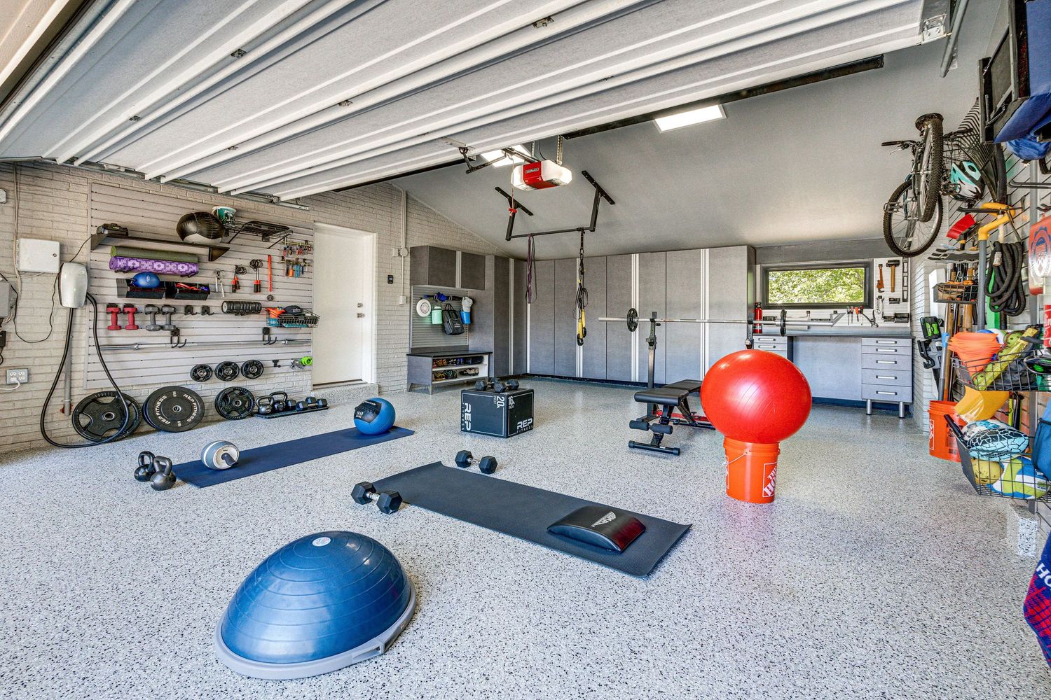 A well-organized residential garage interior with storage shelves, tools, and sporting equipment along the walls.