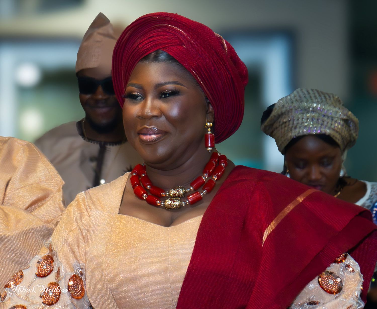 Wedding guest wearing a deep red gele headwrap and cream colored traditional dress with ornate details.