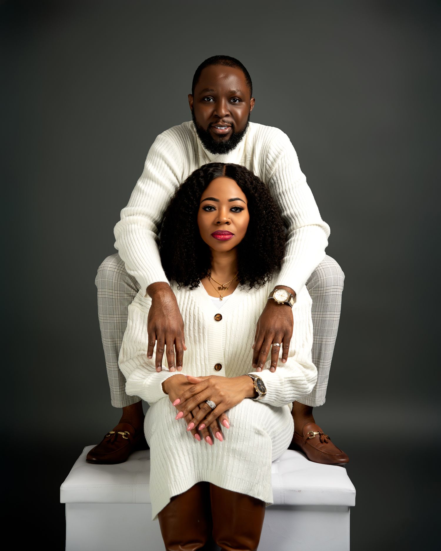 Couple in white sweaters pose intimately in studio portrait setting.