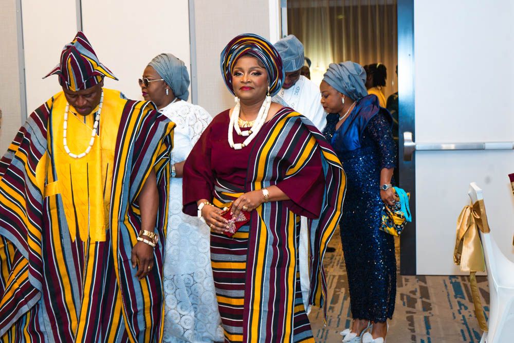 People in vibrant African agbada robes with burgundy and striped patterns at gathering.