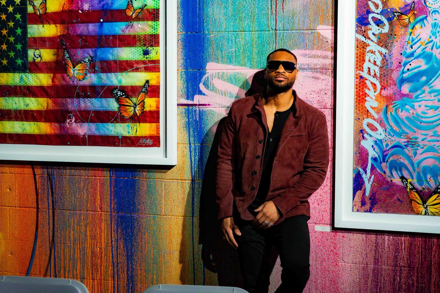 Stylish figure poses against colorful wall with American flag artwork and vibrant graffiti elements.