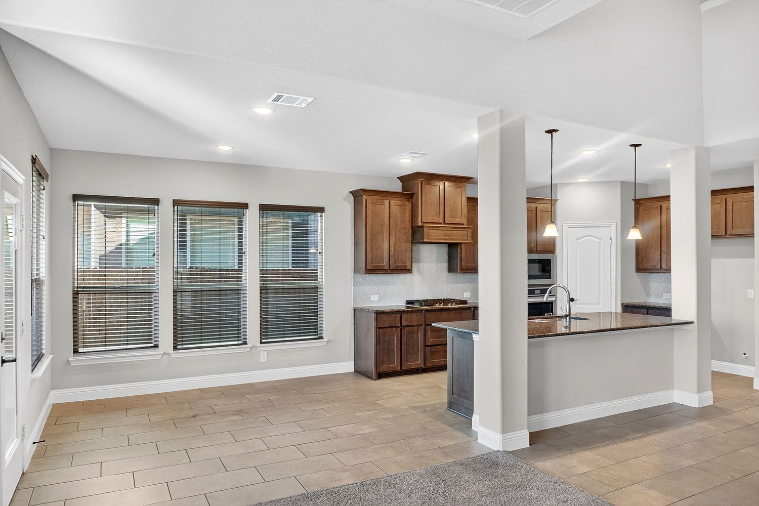 Spacious kitchen and living area with wood cabinets, tile floors, and structural support columns.