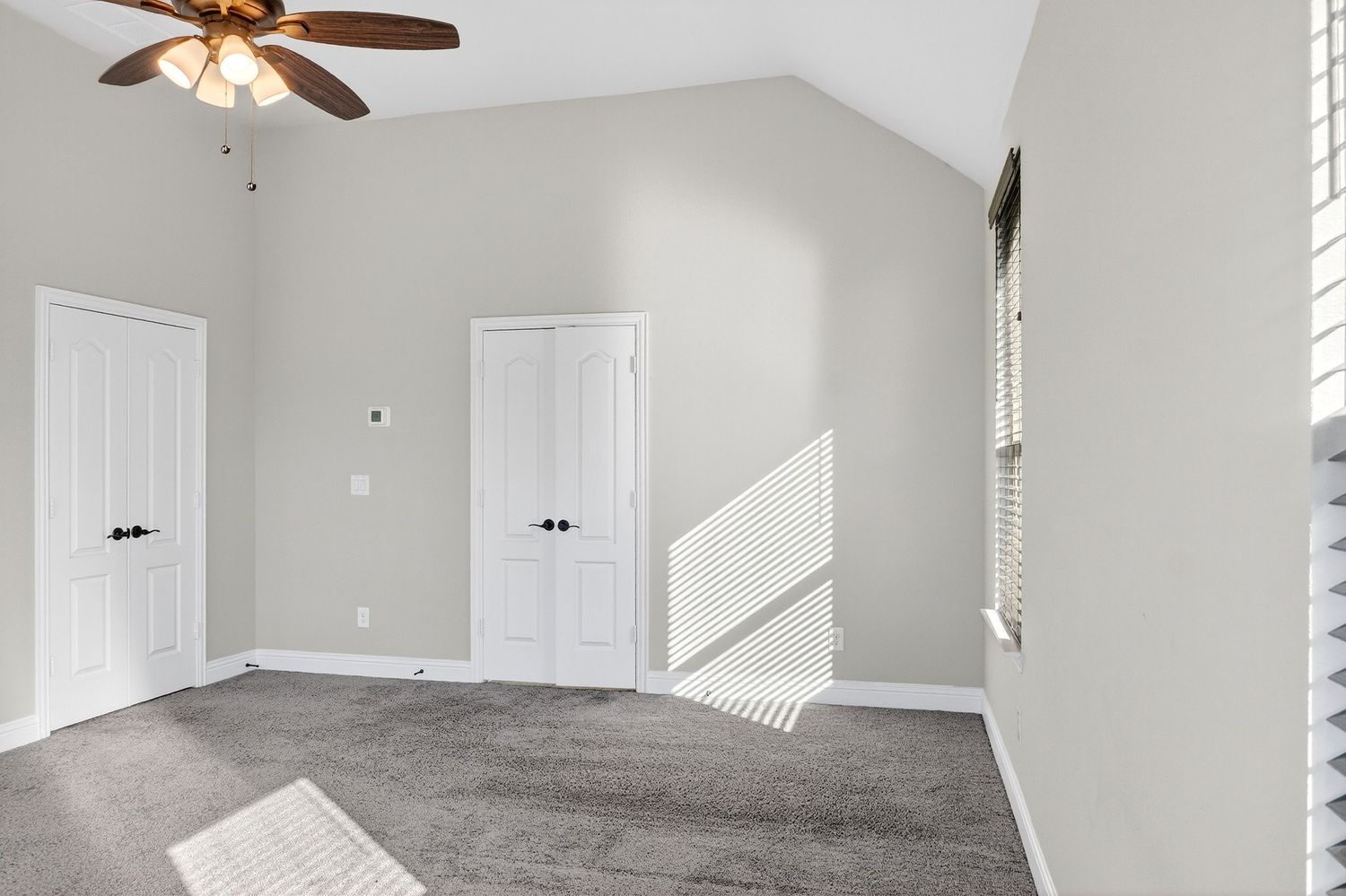 Bedroom with vaulted ceiling, gray carpet, ceiling fan, and two white doors.