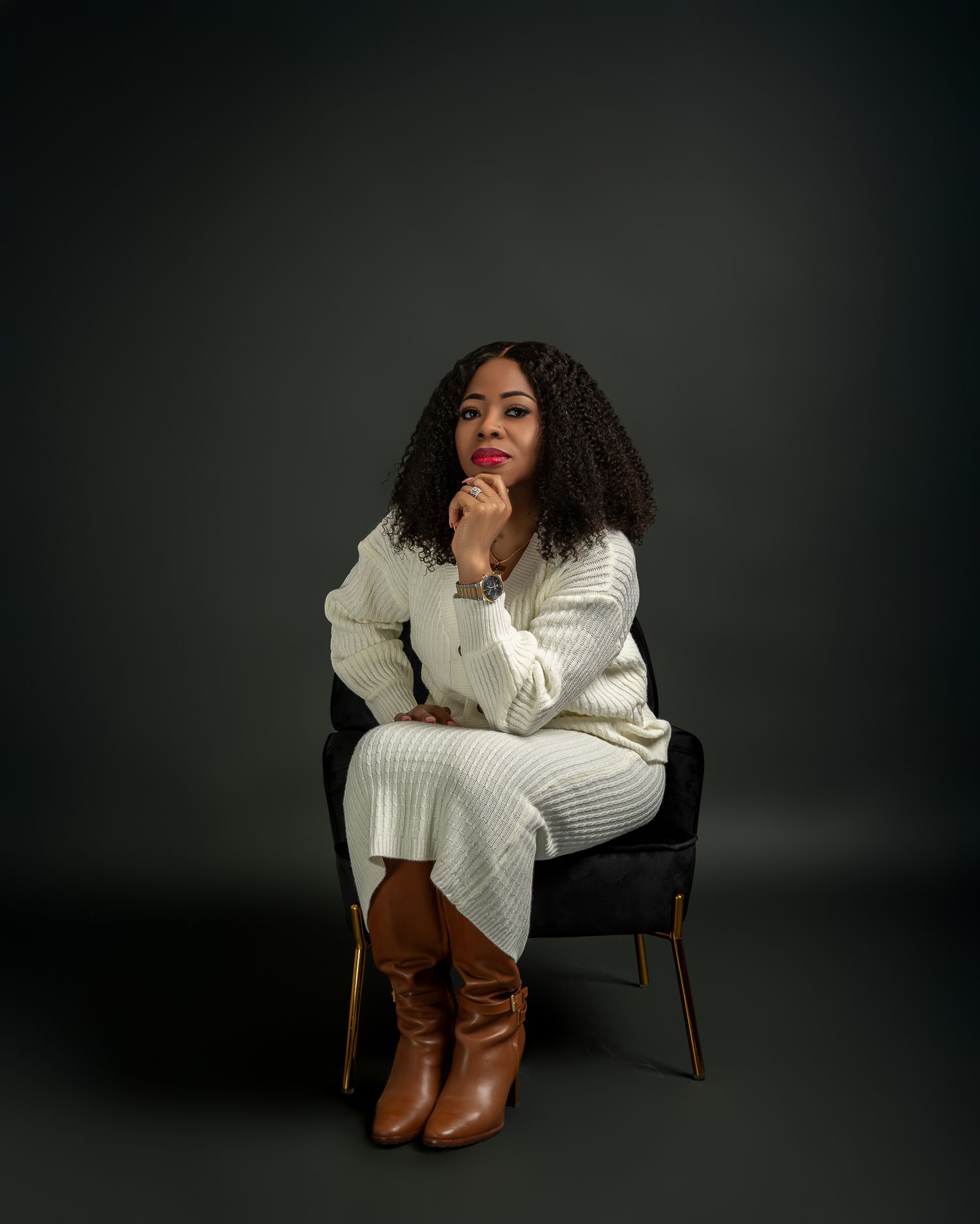 A person in a white knit sweater and brown boots poses elegantly against a dark background.