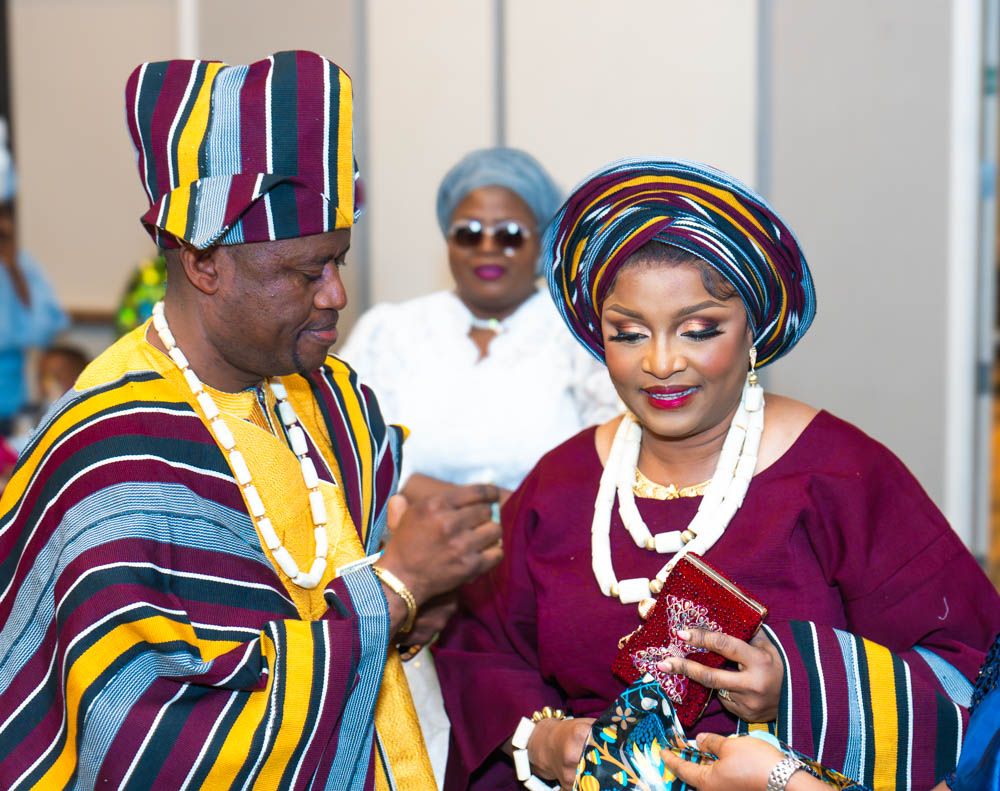 Couple in matching African print attire examining something at formal gathering.