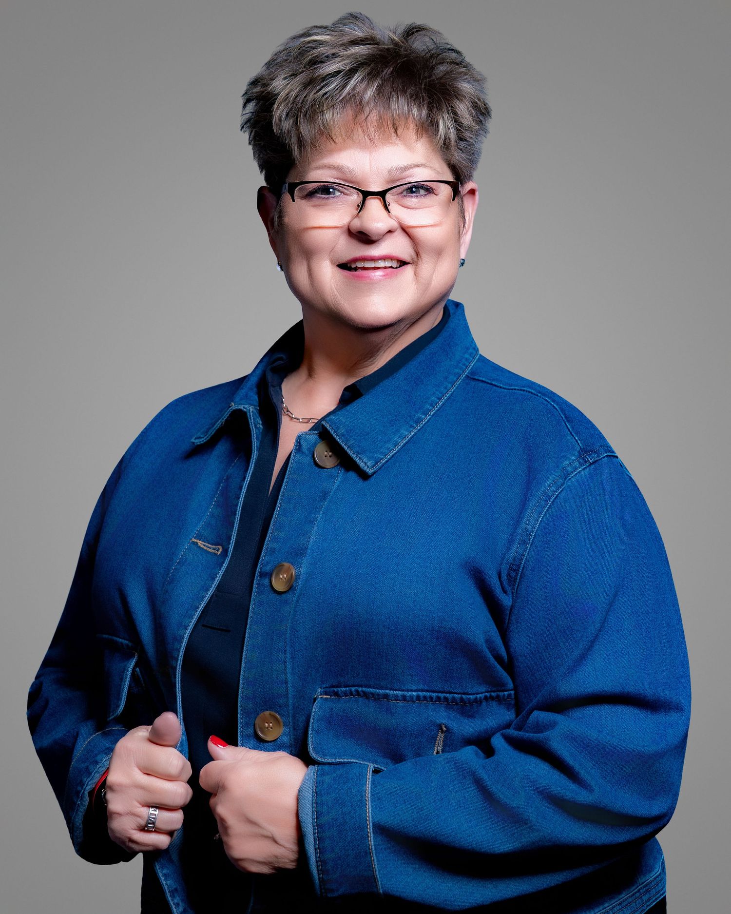 A person wearing glasses and a denim jacket poses in a series of photos against a gray studio background.