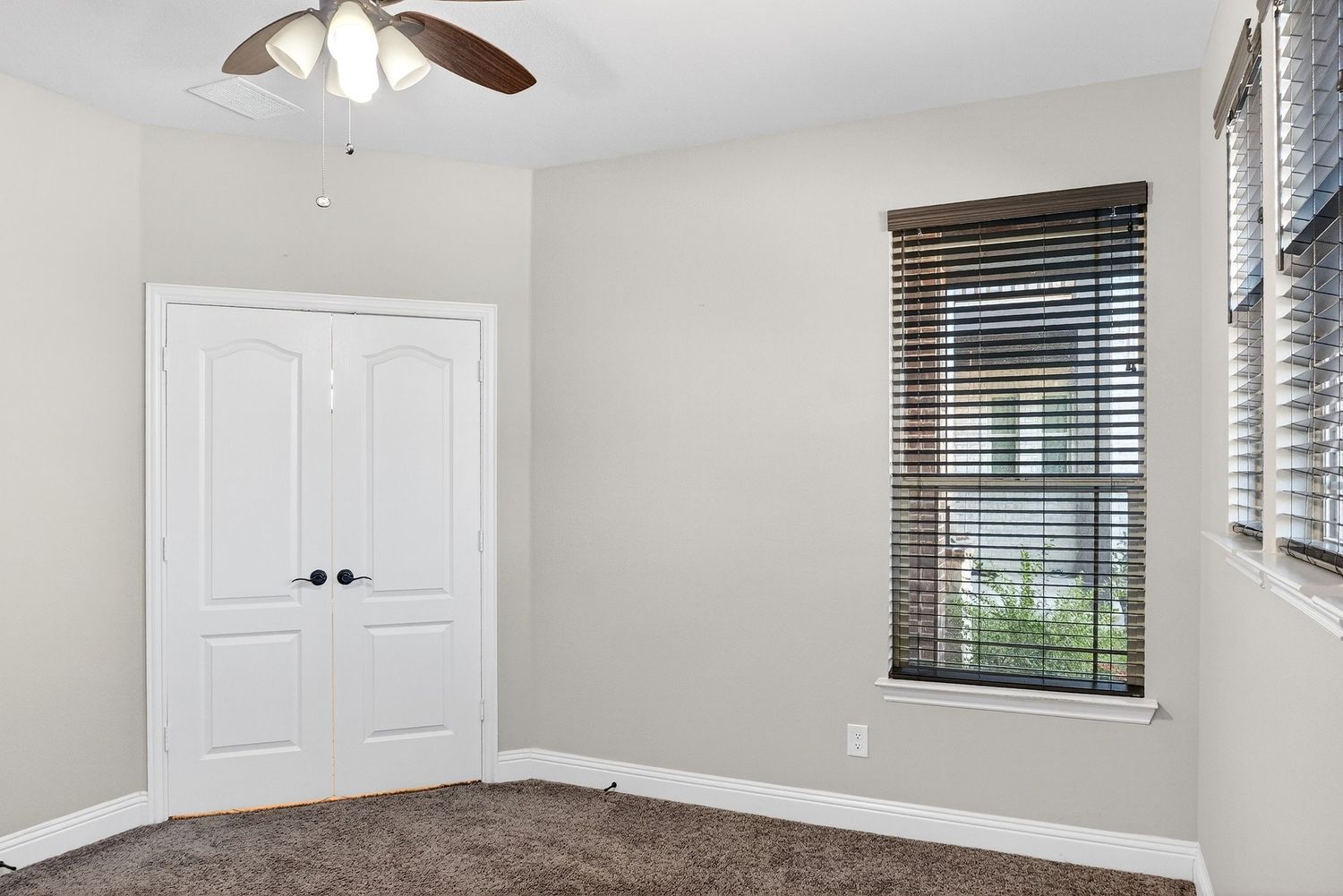 Modern white bedroom interior with ceiling fan, window blinds, and built-in closet storage in bright natural light.