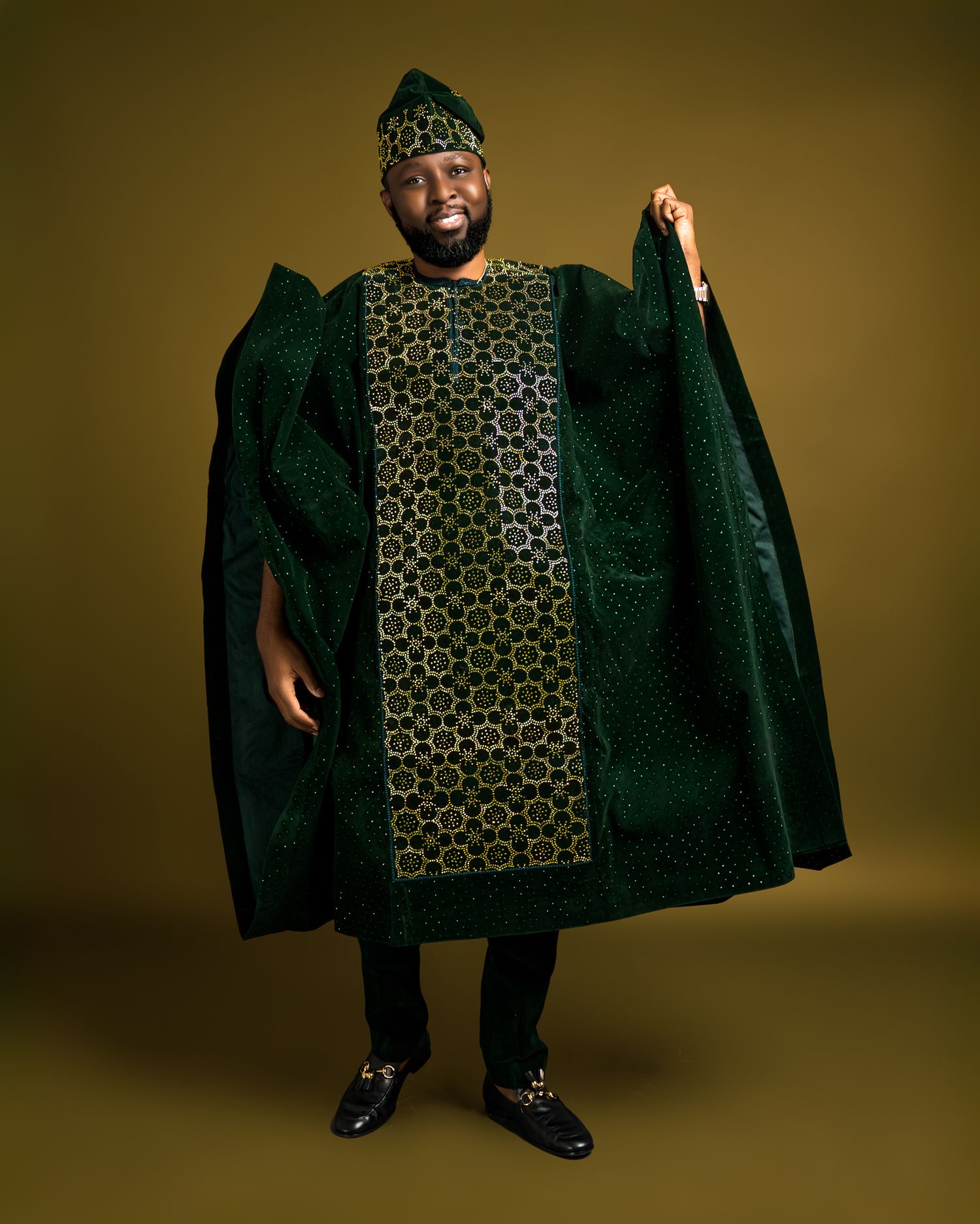 A man wearing an elegant green and gold patterned traditional African agbada poses against gold background.