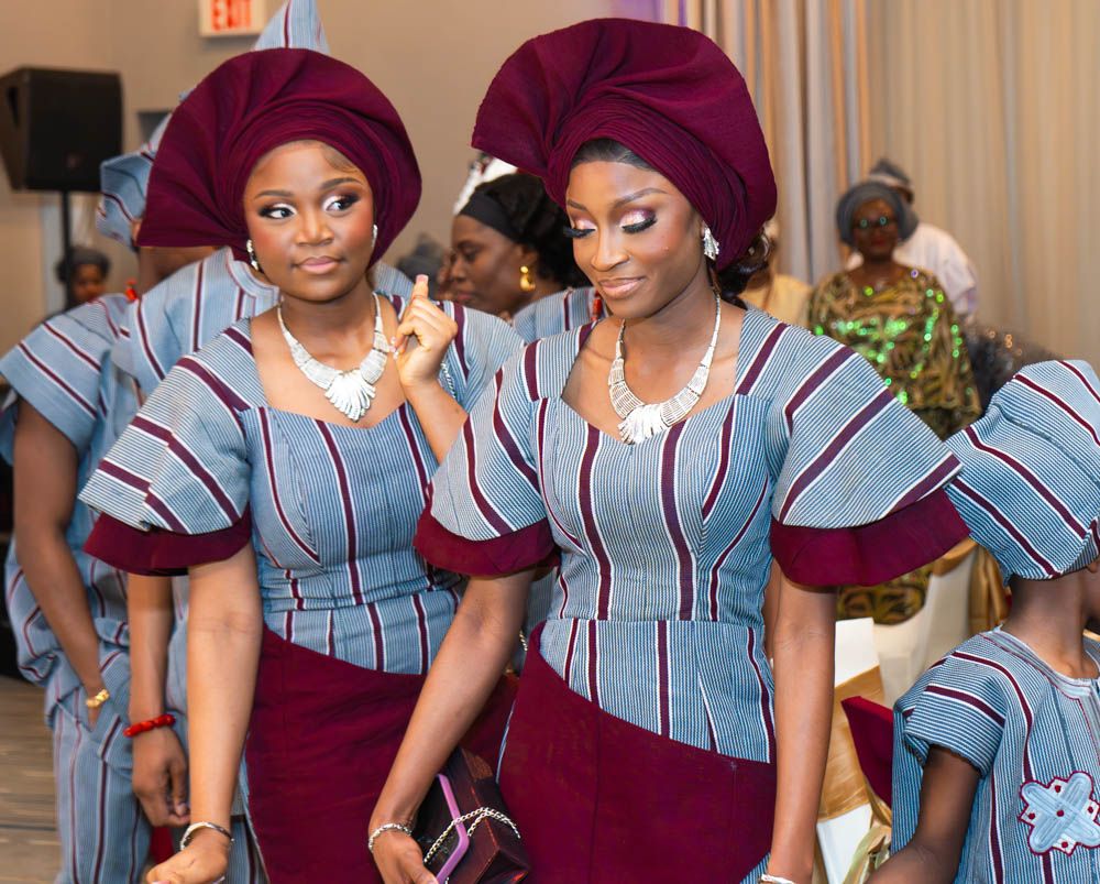 Bridesmaids in coordinating burgundy and blue striped traditional African attire pose at a wedding celebration.