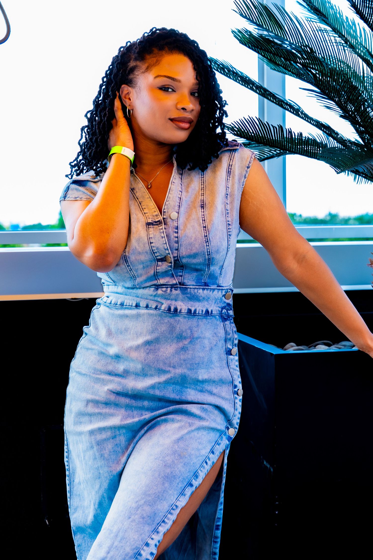 Model in denim outfit posing against palm tree background.