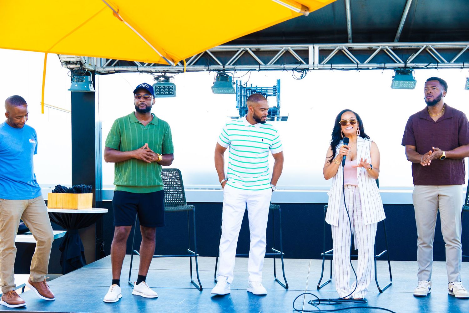 Group of performers standing on stage under a yellow canopy.