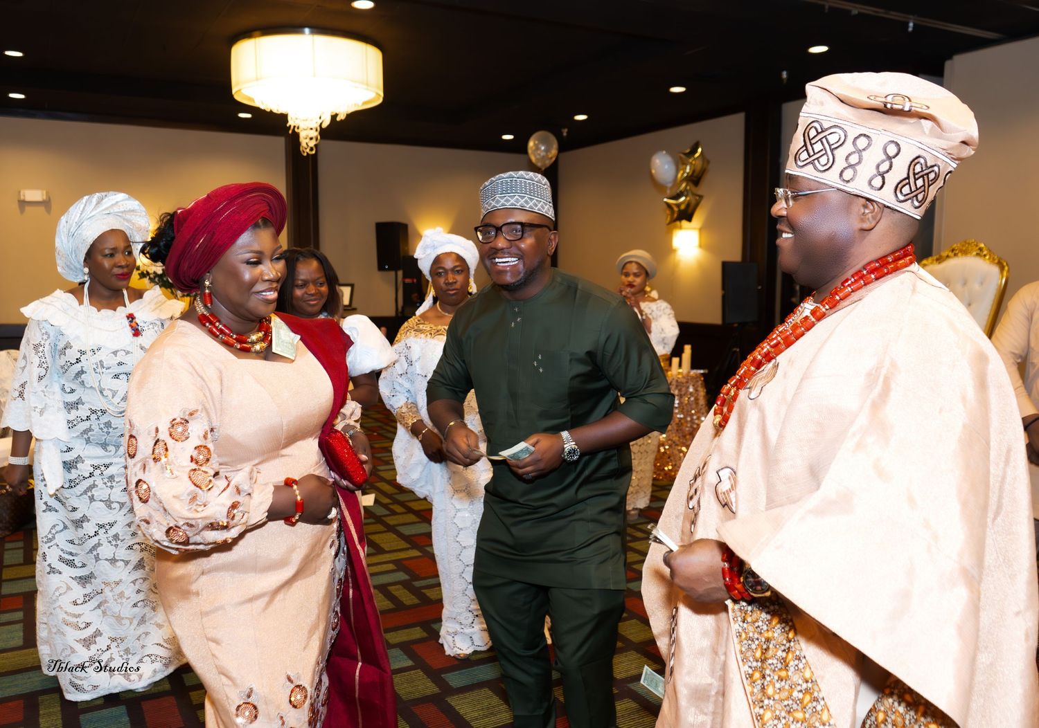 Wedding reception scene with guests in traditional African attire enjoying festivities under indoor lighting.