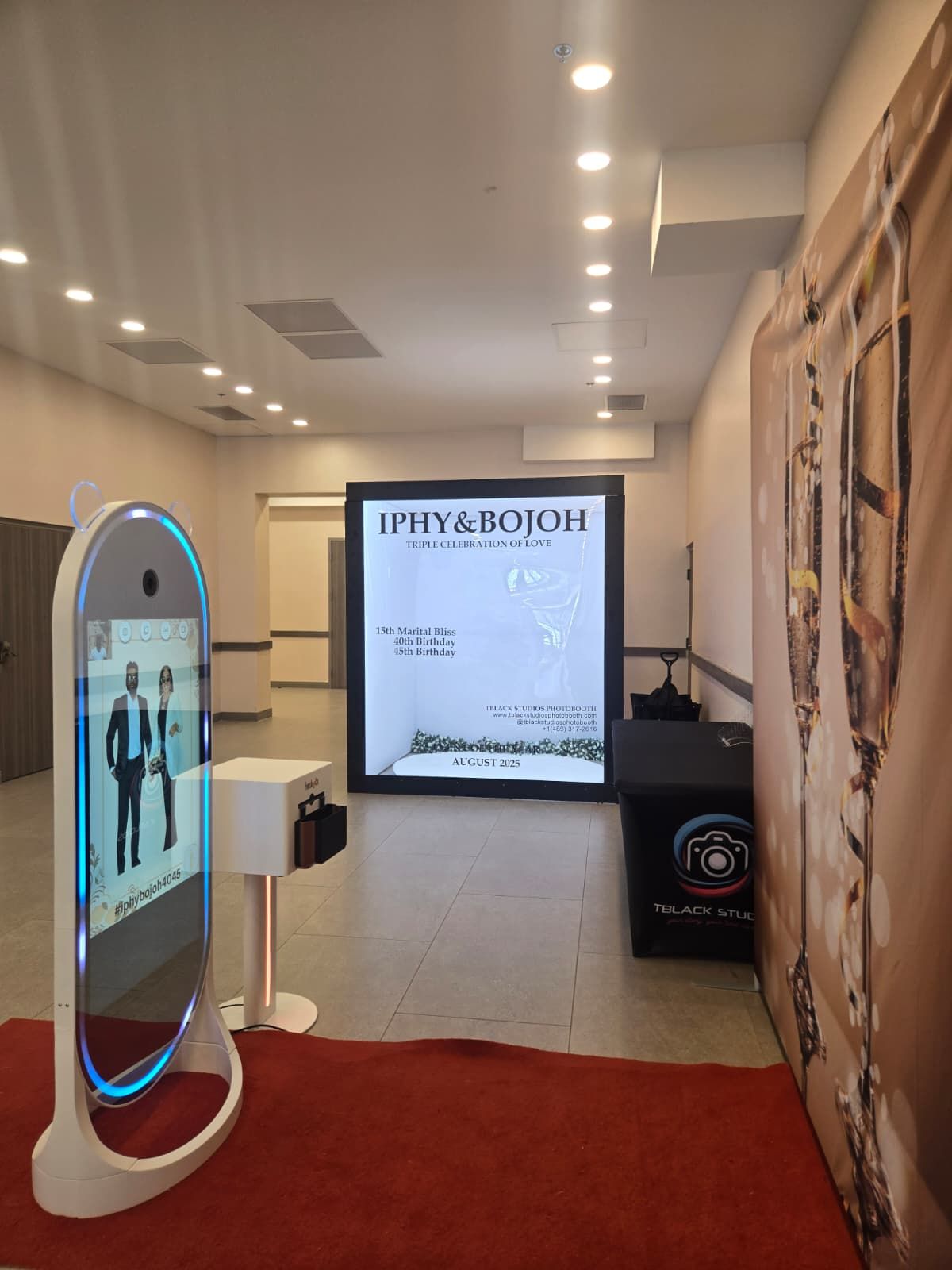 Wide-angle view of photo booth installation in white corridor with digital display screens.