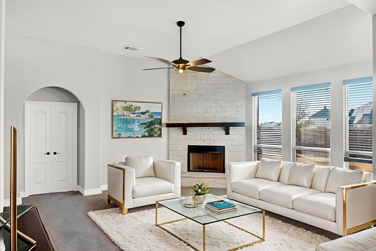Bright open concept living room with white walls, ceiling fan, and large windows.