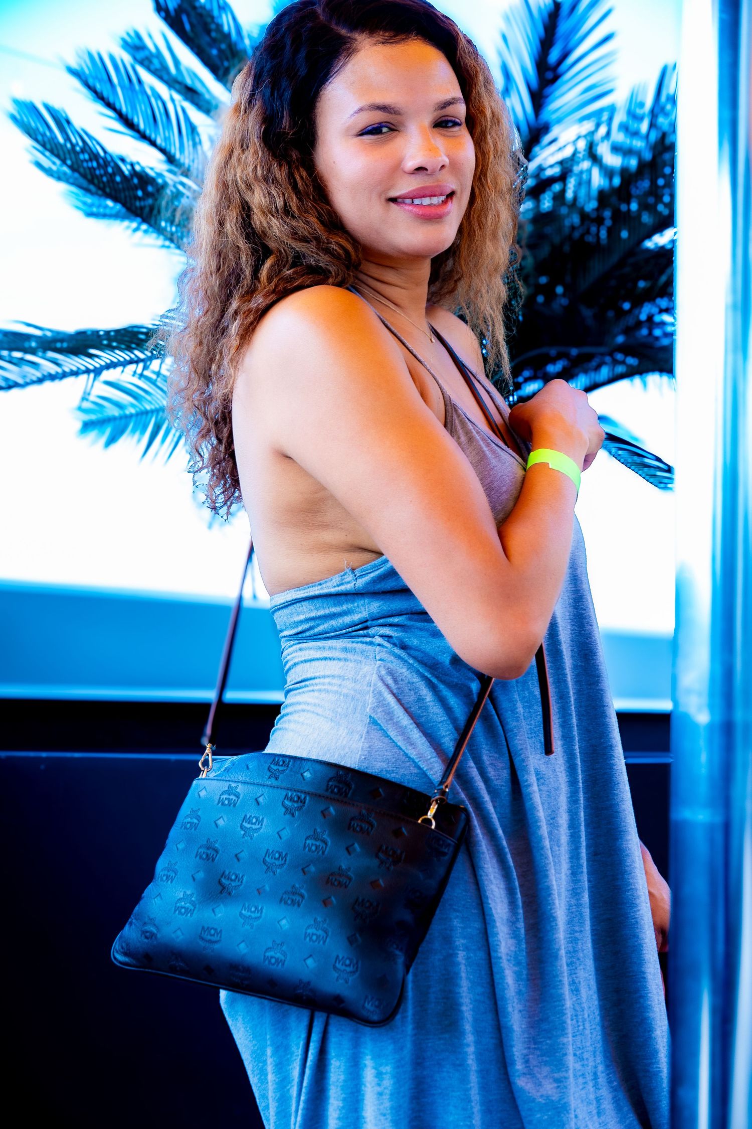 Woman in gray dress with small black purse posing near reflective surface.