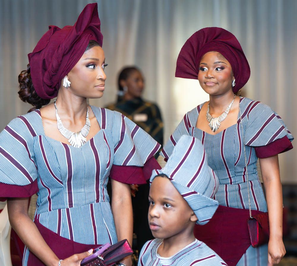 Wedding attendants in coordinated blue striped and burgundy traditional African formal wear pose together.