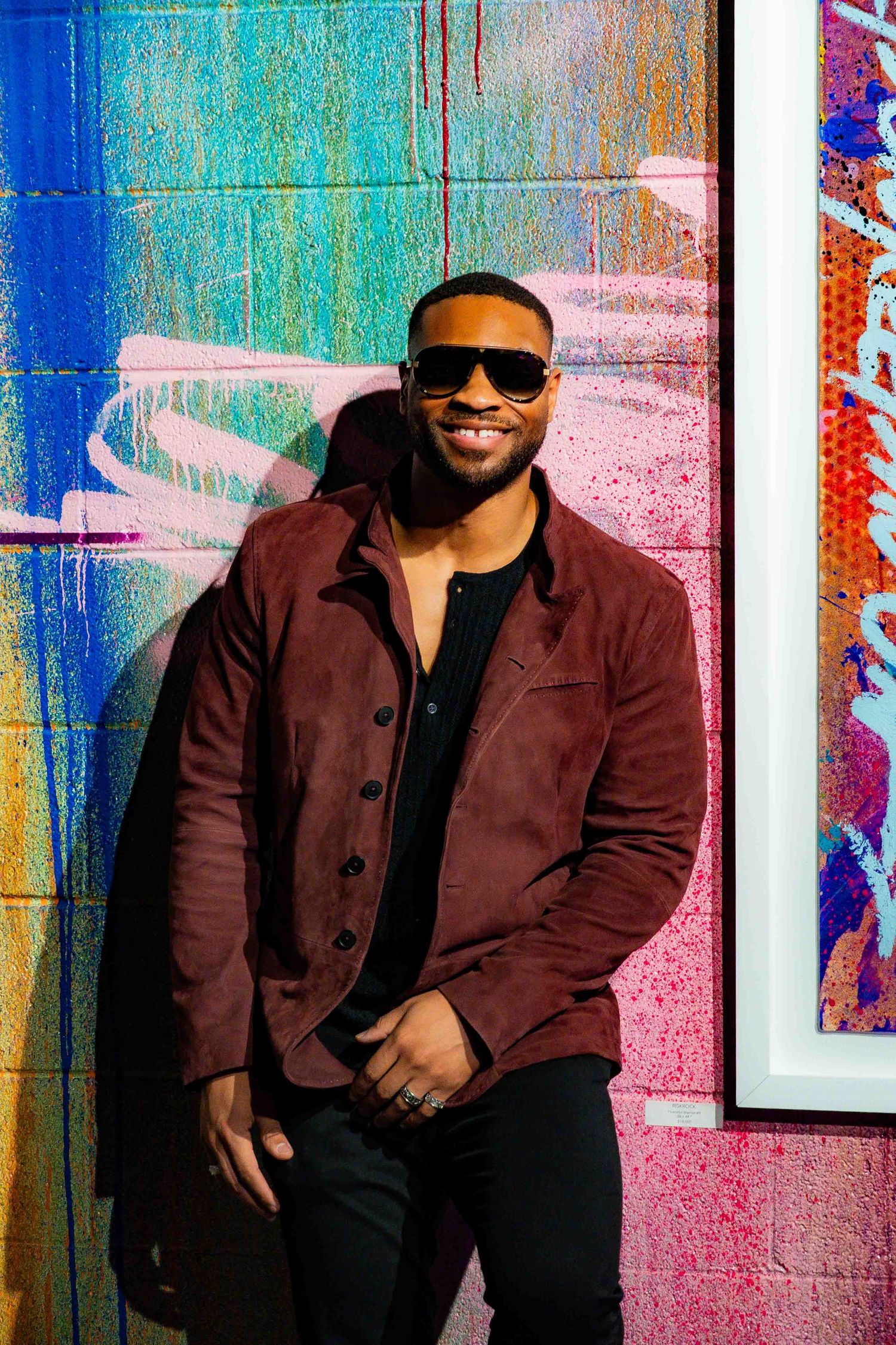 Person in burgundy jacket poses against wall with bright neon colors and framed artwork.