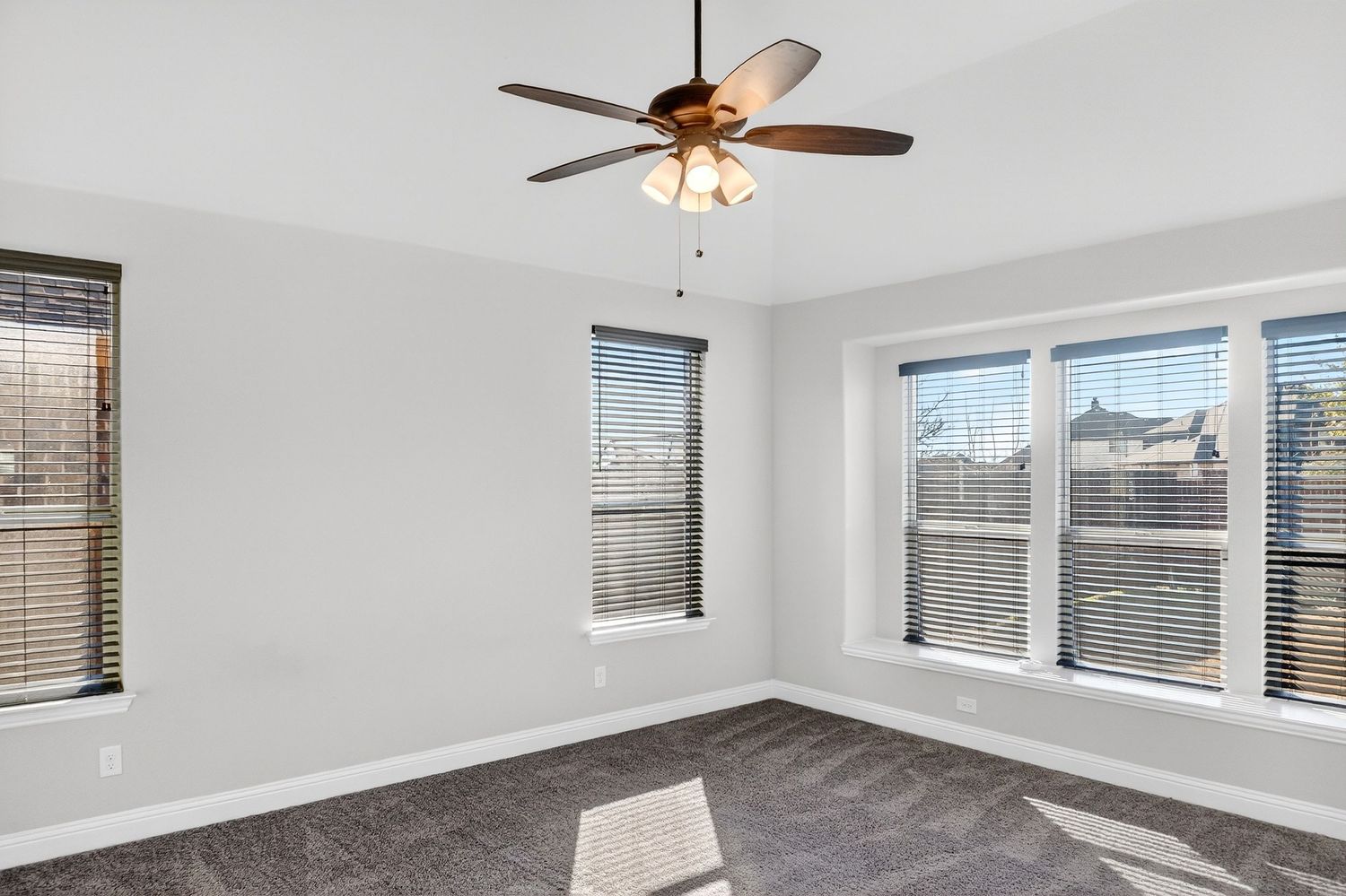 Spacious living area with grey carpet, ceiling fan, and natural light from multiple windows.