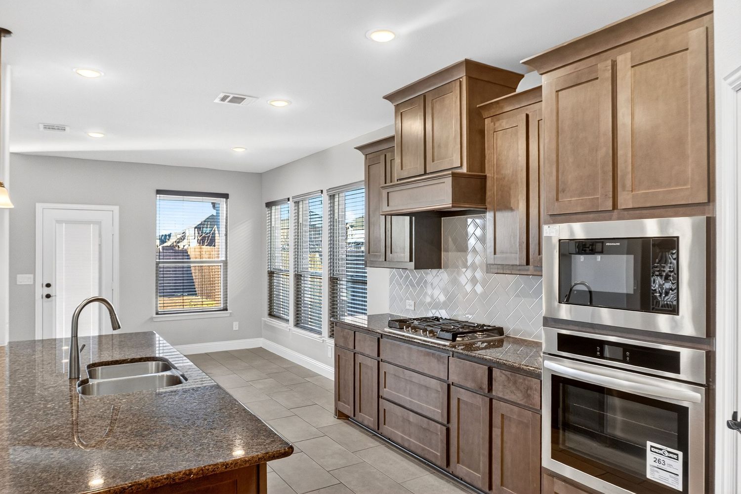 Modern kitchen with brown cabinets, granite countertops, and stainless steel appliances.