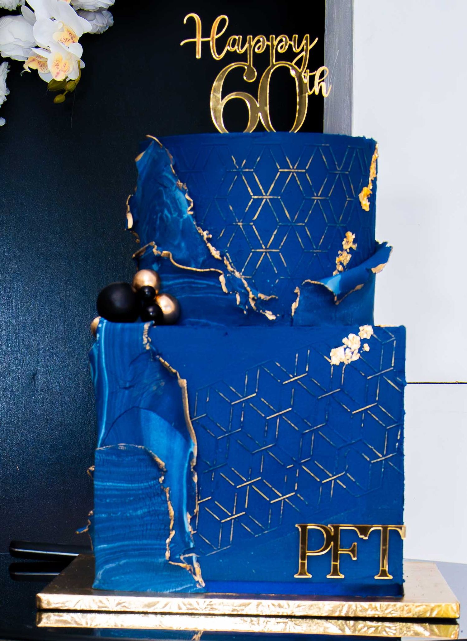 Elegant blue tiered celebration cake with gold accents and geometric pattern details.