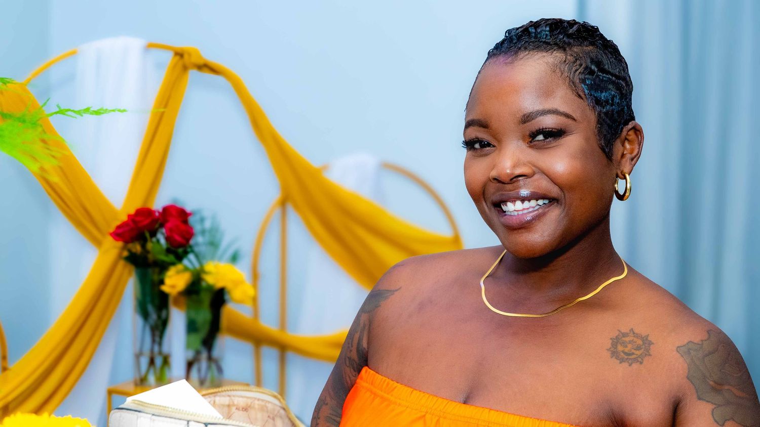 Model in yellow dress poses with decorative yellow fabric and floral arrangements.