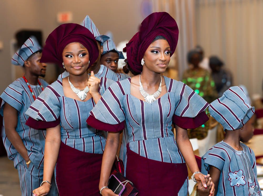 Women in matching burgundy and striped traditional African dresses at cultural event.