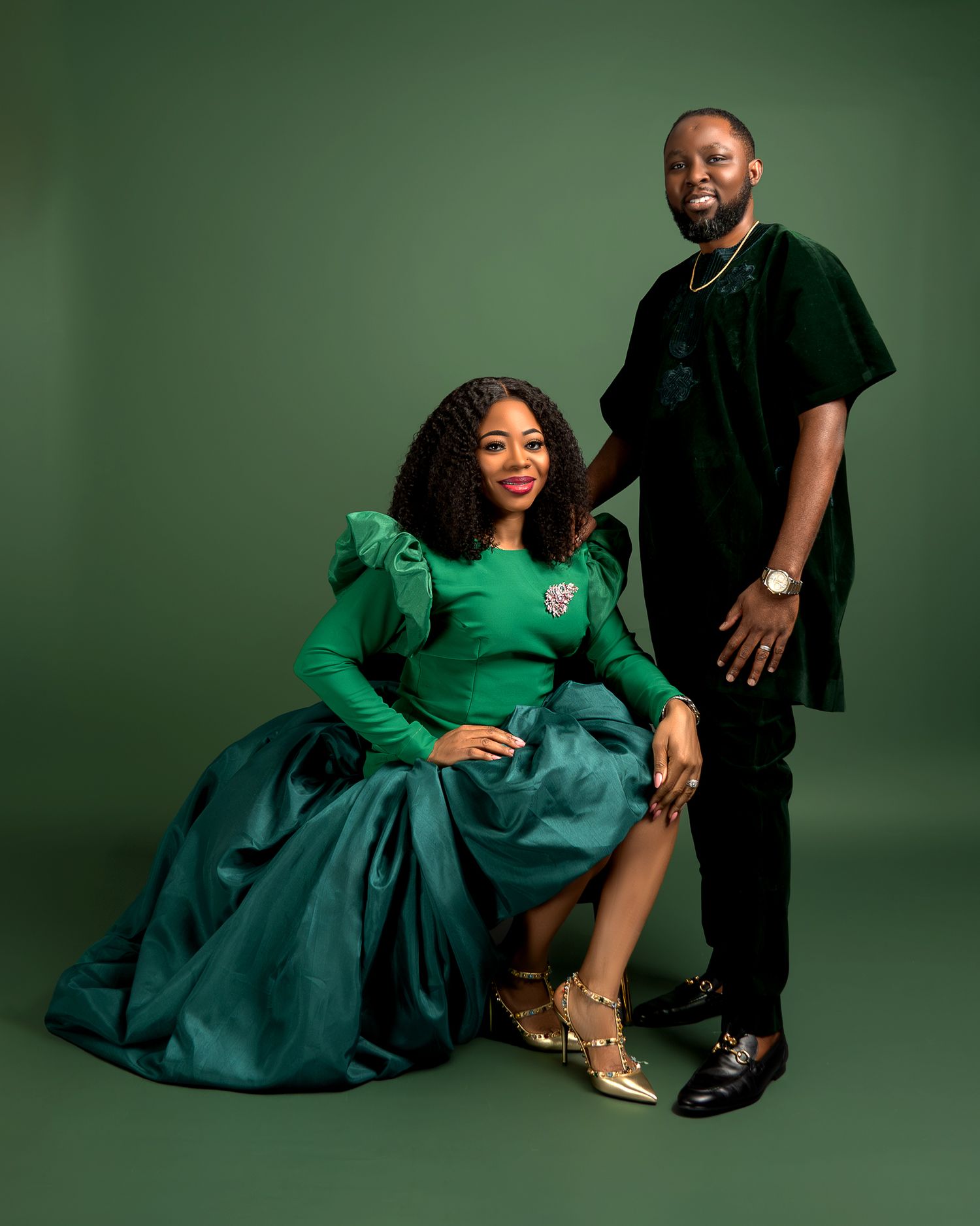 A glamorous photoshoot featuring a flowing emerald green dress against a dark green backdrop.