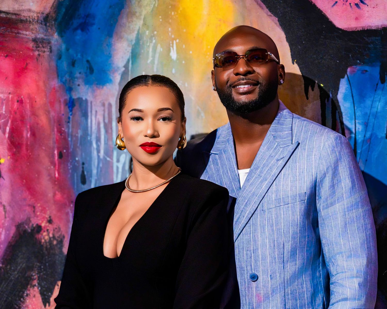 Couple's portrait session with blue suit and black dress against artistic wall.