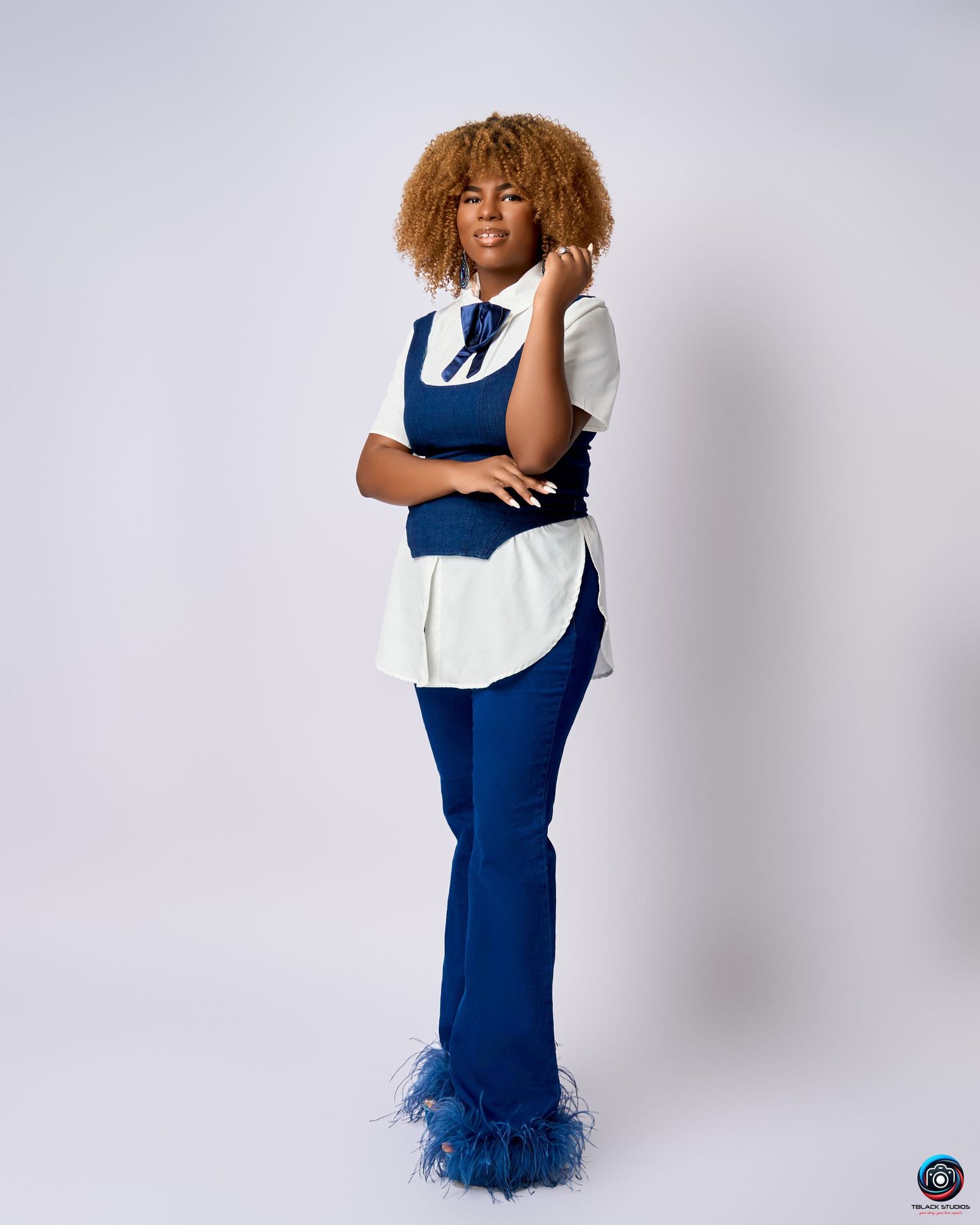 Model in blue dress and white top poses expressively in studio photoshoot.