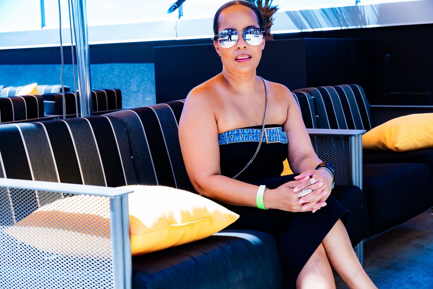 Woman in black dress sitting on dark couch with yellow pillows.