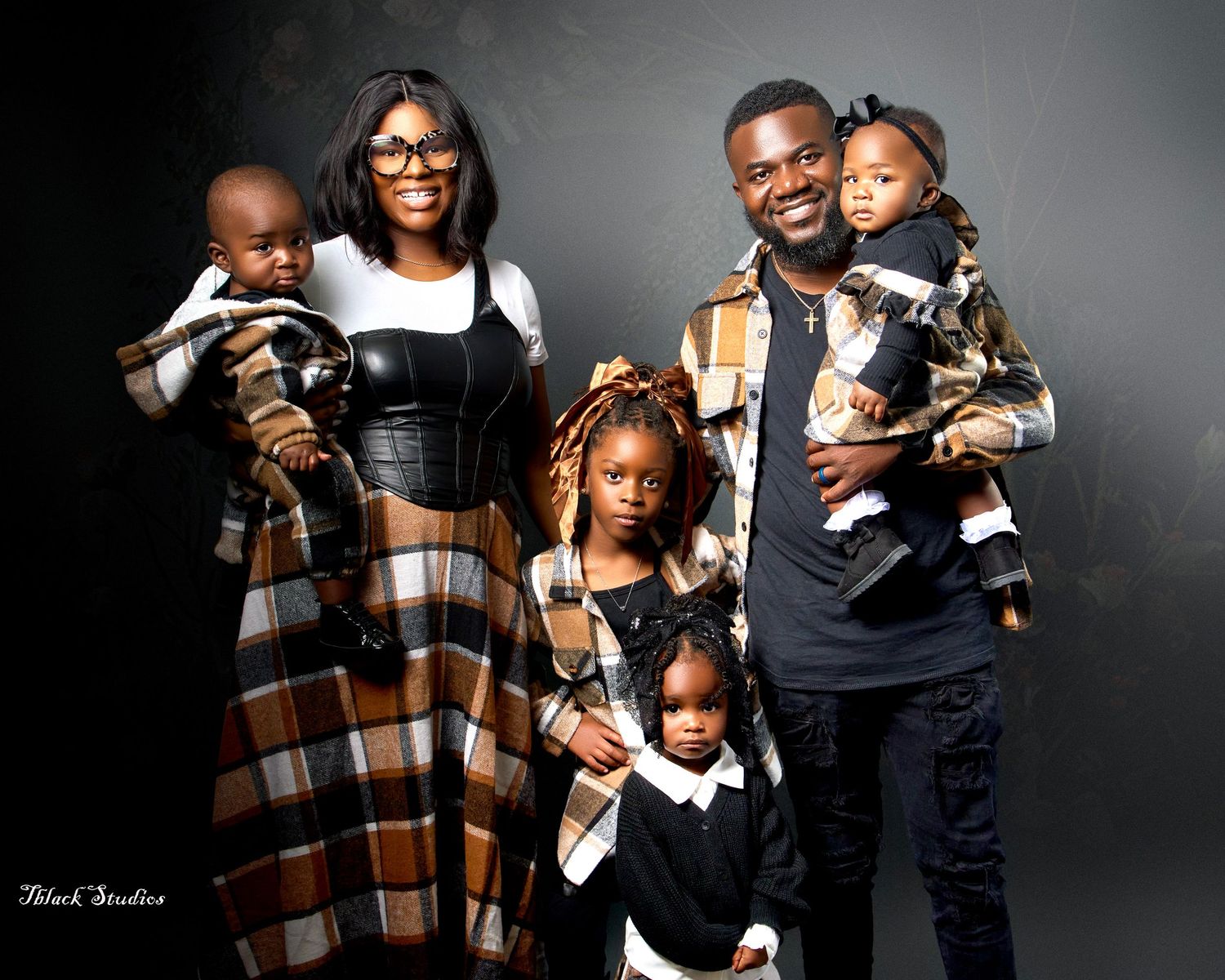 Studio family portrait session with coordinated brown plaid and black outfits.