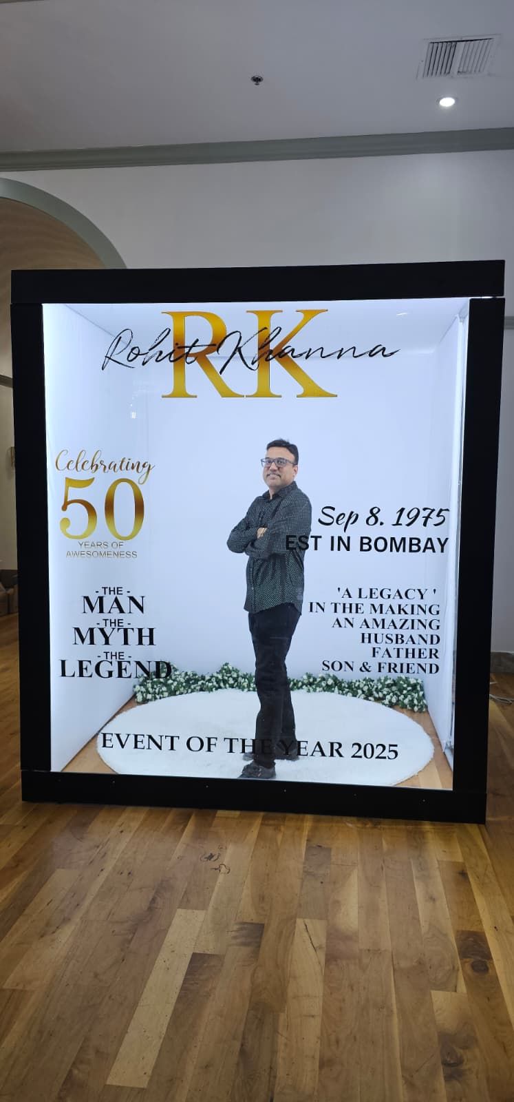 Large display sign celebrating 50 years with RK branding, gold text, and floral decor on white backdrop in an event space.