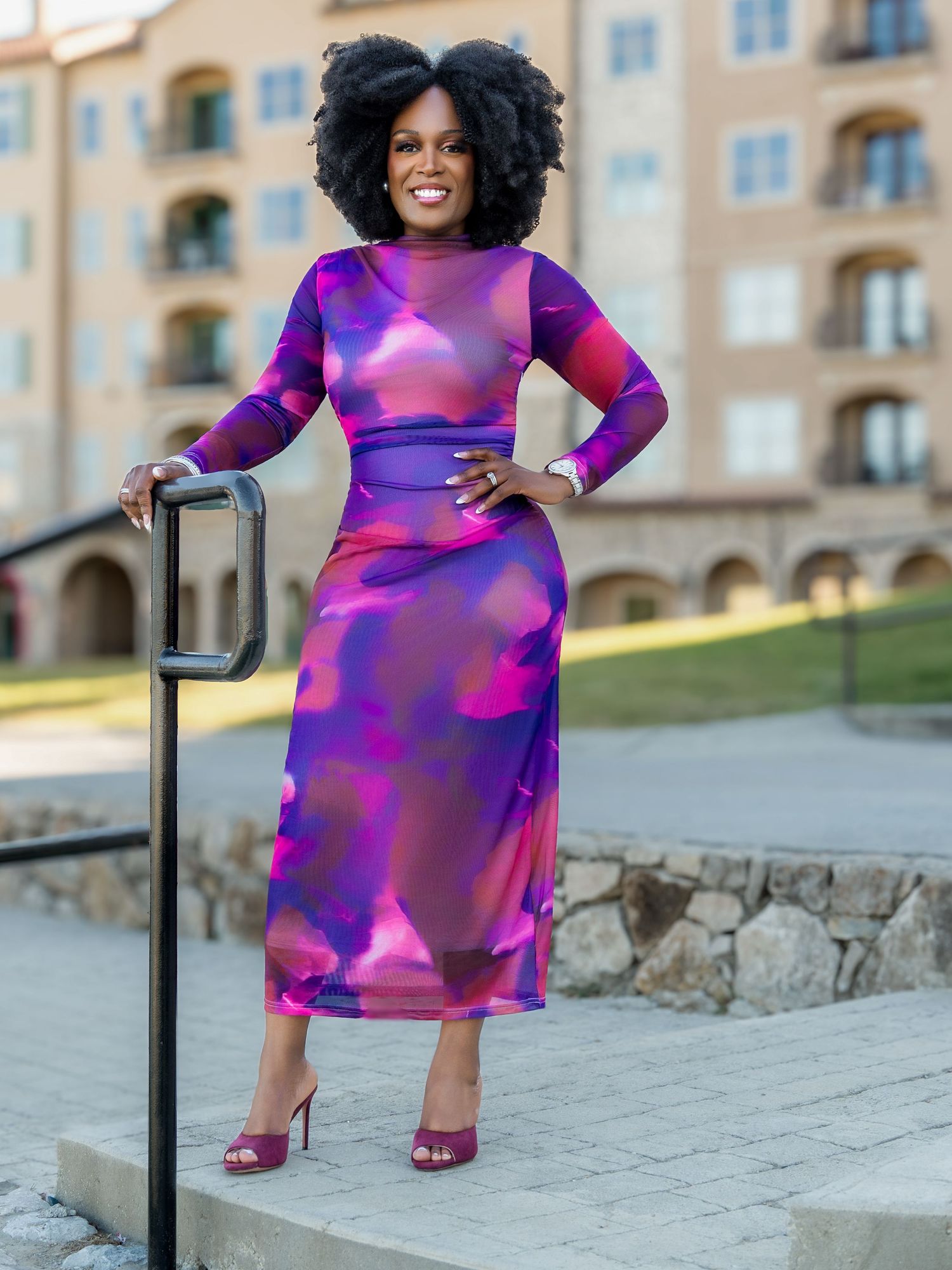 Vibrant purple and pink patterned dress photographed against stone architecture in an outdoor photoshoot.