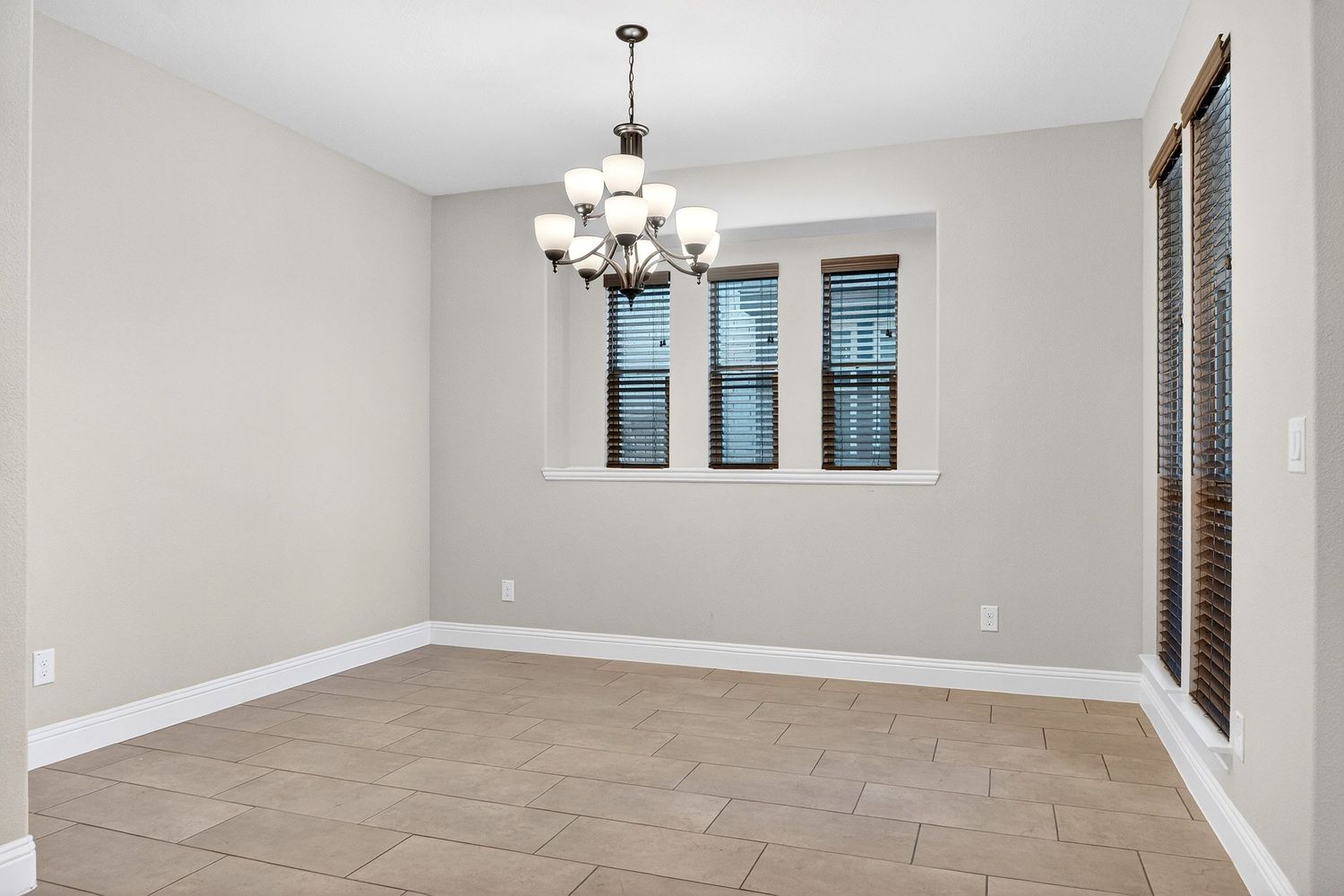 Empty room with gray walls, wood-look tile flooring, and a modern chandelier hanging from white ceiling.